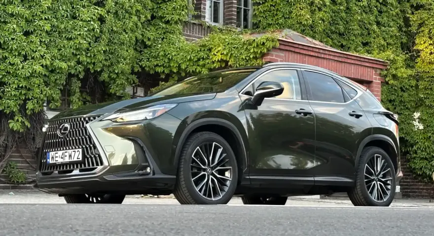 Ciemnozielony Lexus NX 450h+ plug-in zaparkowany przed budynkiem porośniętym bluszczem.