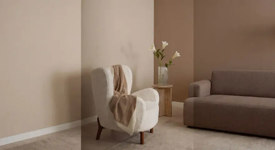 Gemütliches Wohnzimmer mit beigen und braunen Wandfarben. Ein flauschiger Sessel mit Decke und ein Sofa laden zum Entspannen ein.