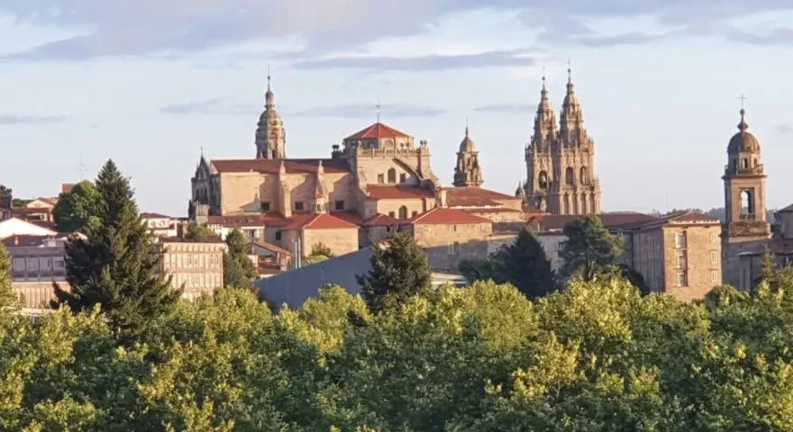 Majestatyczna katedra w Santiago de Compostela, cel pielgrzymek, wyłania się zza zieleni drzew.