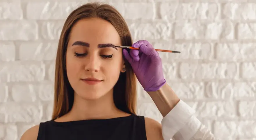Korekta zbyt ciemnej henny na brwiach. Stylistka nakłada produkt rozjaśniający.