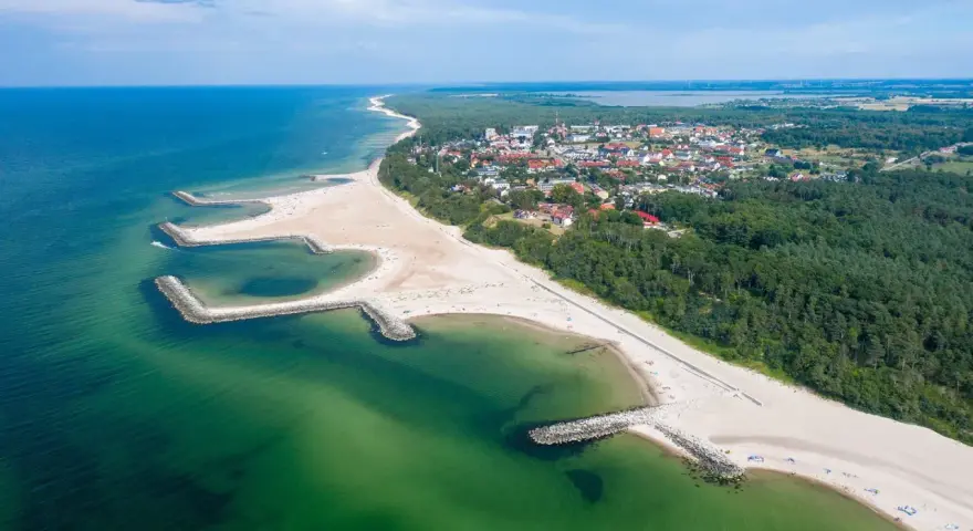 Malownicze plaże w Polsce z kamiennymi falochronami, zielonymi wodami Bałtyku i nadmorskim miasteczkiem w tle.