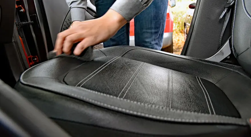 Hand reinigt Autositz aus Leder mit einem Tuch. Hausmittel für Leder reinigen sind eine gute Wahl.