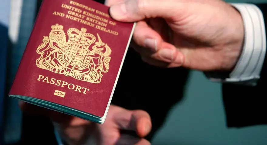 Dłoń podaje paszport biometryczny Wielkiej Brytanii. Widoczny herb i napis "PASSPORT".