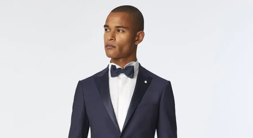 Uomo con smoking blu scuro, camicia bianca e papillon blu. Un look elegante per ogni occasione speciale.