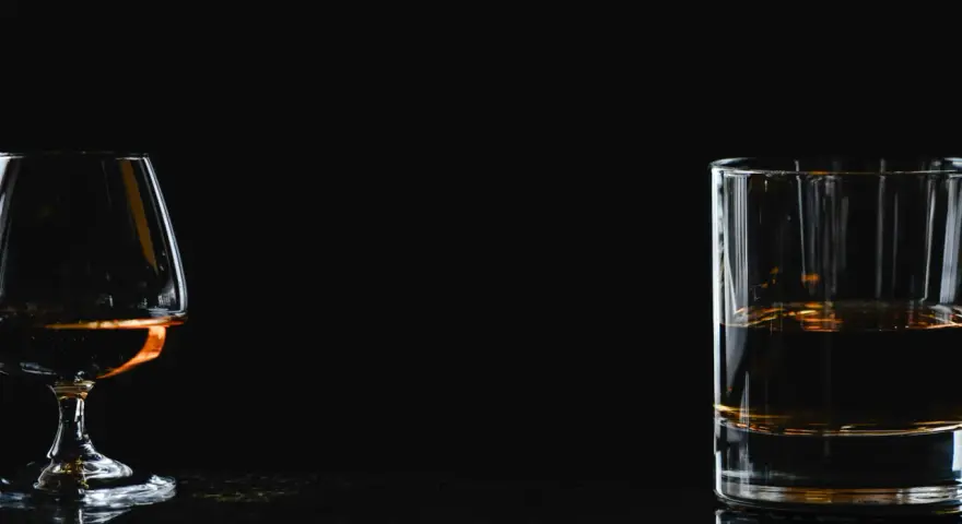 Kieliszek z brandy i szklanka z whisky na ciemnym tle.