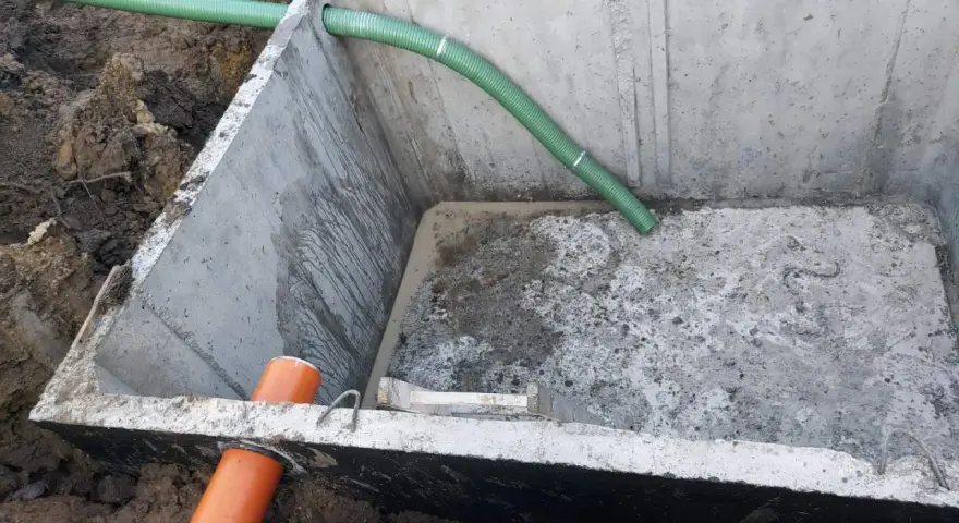 Montaż szamba betonowego 10m3. Widoczny betonowy zbiornik w wykopie, z podłączonymi rurami.