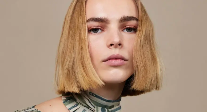 Modelka z subtelnym makijażem i fryzurą bob krótki tył, prezentuje się elegancko w bluzce z wzorem.