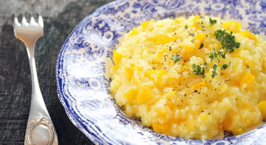 Pyszny, kremowy ryż do risotto z kawałkami dyni, posypany świeżym tymiankiem i pieprzem. Obok leży ozdobny widelec.