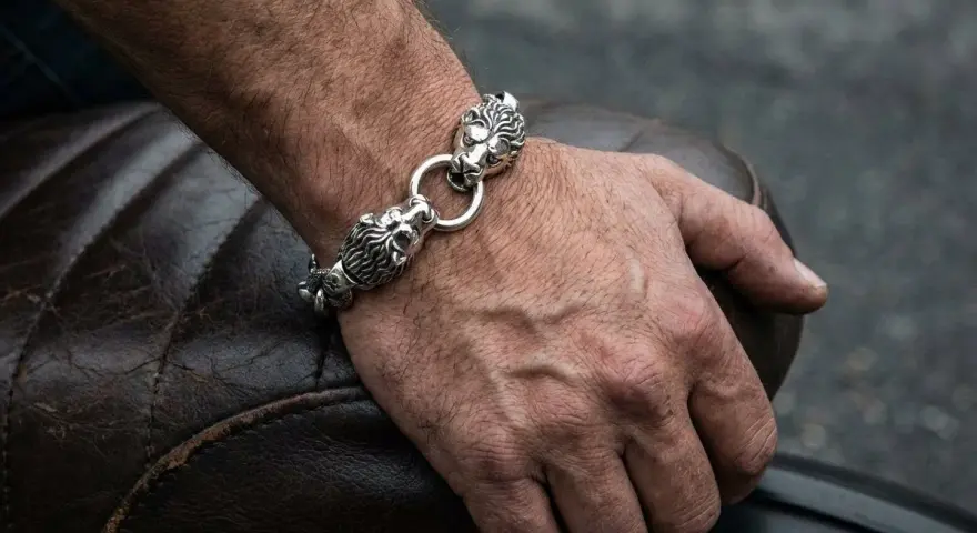 Męska dłoń z bransoletą z lwimi głowami, symbolizującą gest, kiedy mężczyzna daje kobiecie biżuterię.