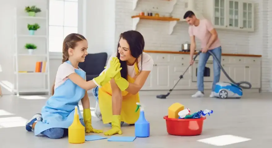 Mama i córka świętują wykonane obowiązki 9 latka w domu. Tata odkurza w tle.