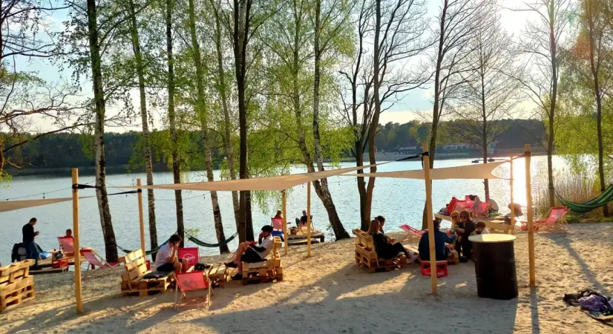 Relaks na piaszczystej plaży nad jeziorem. Ludzie odpoczywają w cieniu namiotów, tworząc przytulne pola namiotowe nad jeziorem.