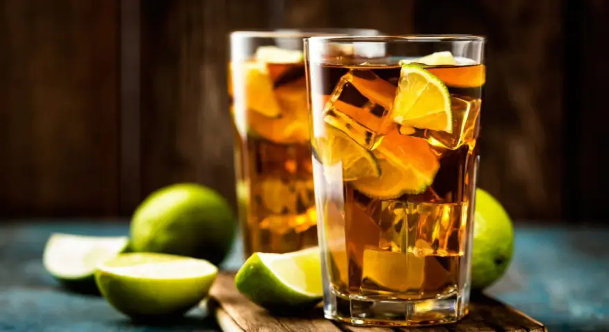 Dwa orzeźwiające drinki: Long Island Iced Tea czy Tokyo Tea, z lodem i limonką, na drewnianej desce.