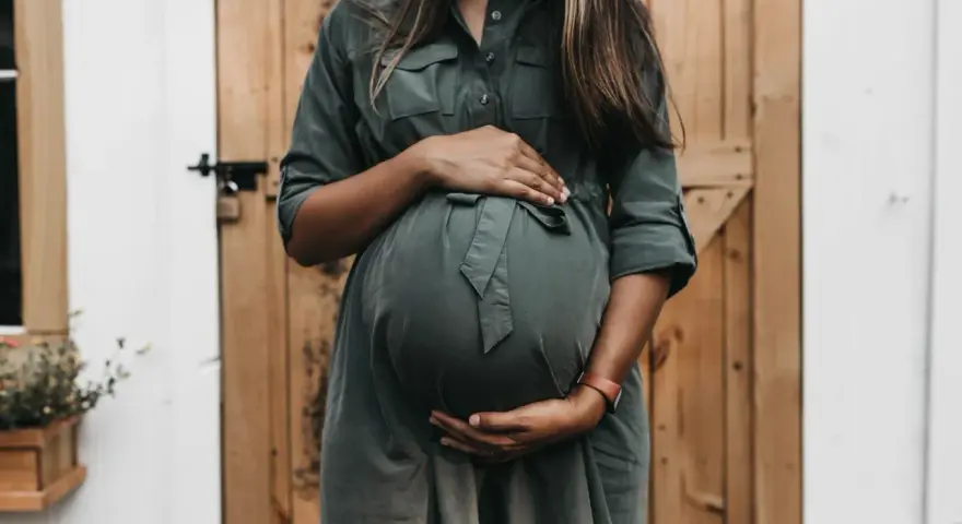 Kobieta w zielonej sukience obejmuje ciążowy brzuch. Czy to tokofobia co to?