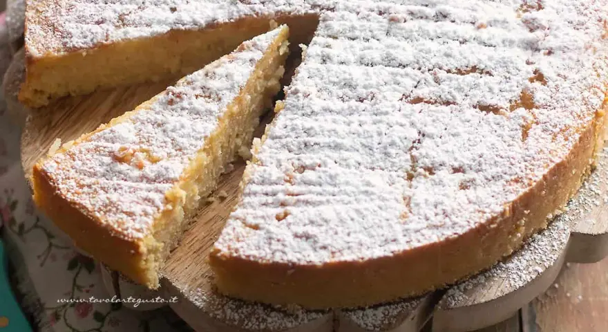 Una deliziosa torta di riso, cosparsa di zucchero a velo, su un tagliere di legno. Una fetta è già stata servita.