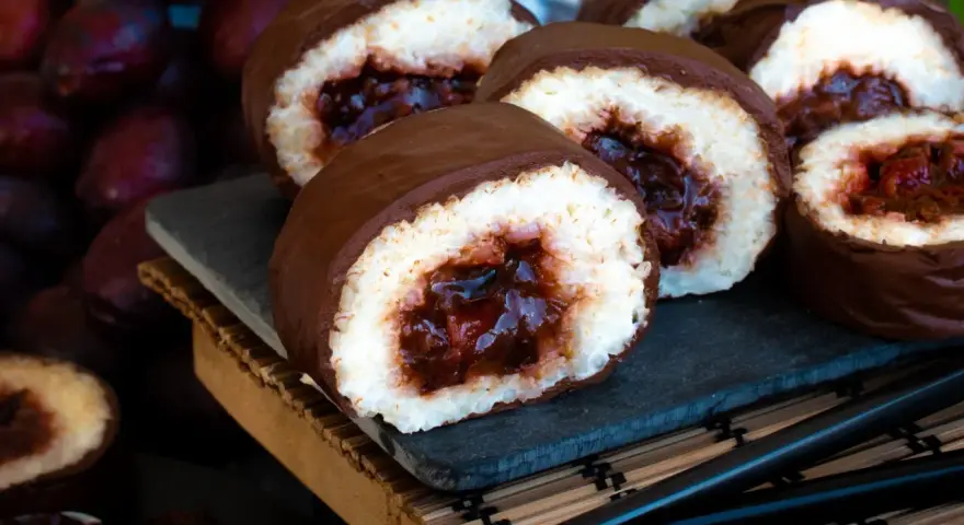 Słodkie rolki sushi na słodko, oblane czekoladą, z owocowym nadzieniem. Obok ciemne owoce i pałeczki.