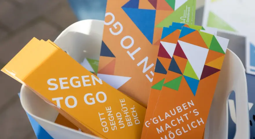 Bunte Karten mit der Aufschrift "Segen to go" und inspirierenden Botschaften wie "Gott segne und behüte dich" liegen in einem Korb.