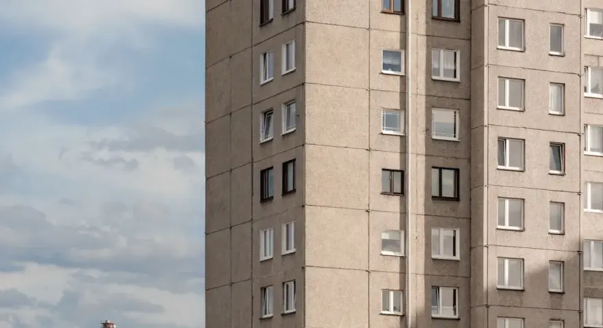 Szare bloki mieszkalne, każde mieszkanie od miasta z oknami wychodzącymi na niebo. W oddali widać komin.