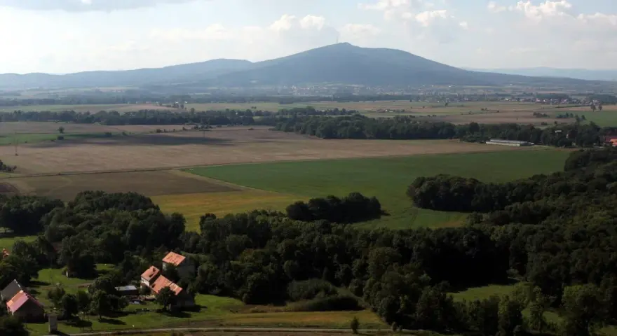 Widok na górzystą okolicę obok Wrocławia z polami, lasami i kilkoma domami.