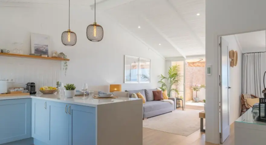 Cocina y sala de estar luminosas, perfectas para decorar casa playa poco presupuesto. Muebles claros, plantas y detalles náuticos crean un ambiente fresco.
