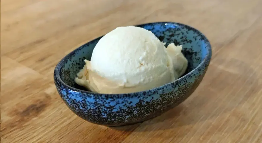 Ein Löffel cremiges Mandel Eis in einer blauen Schale auf Holztisch.