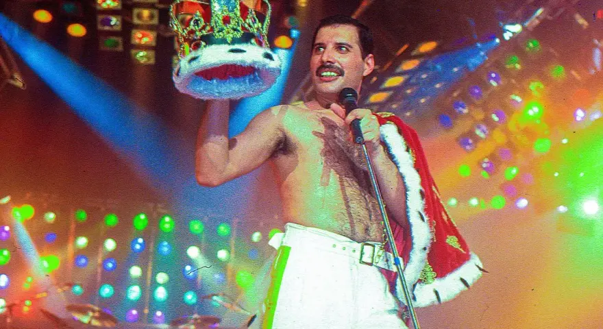 Freddie Mercury, król sceny, w koronie i z mikrofonem, na tle kolorowych świateł.