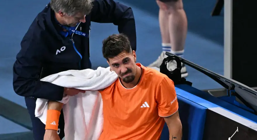 Tenisista z pomarańczową opaską na przedramieniu podczas Australian Open 2024 otrzymuje pomoc od fizjoterapeuty.