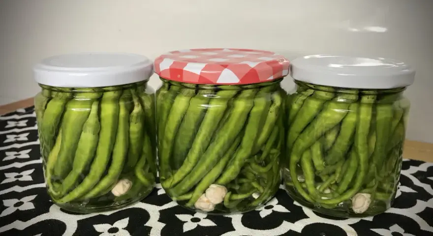 Tres frascos de vidrio llenos de piparras en vinagre, con ajos en el fondo. Uno tiene tapa a cuadros rojos y blancos.