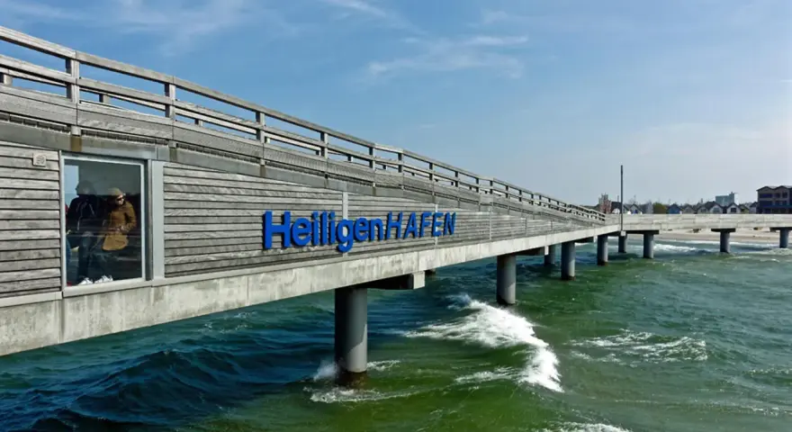 Hol dir die besten heiligenhafen tipps! Die Seebrücke mit dem Schriftzug "Heiligenhafen" ragt ins grüne Meer.