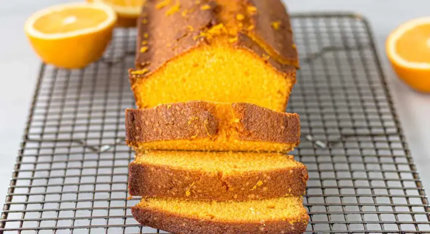 Un delicioso bizcocho de naranja, recién horneado y cortado en rebanadas, reposa sobre una rejilla.