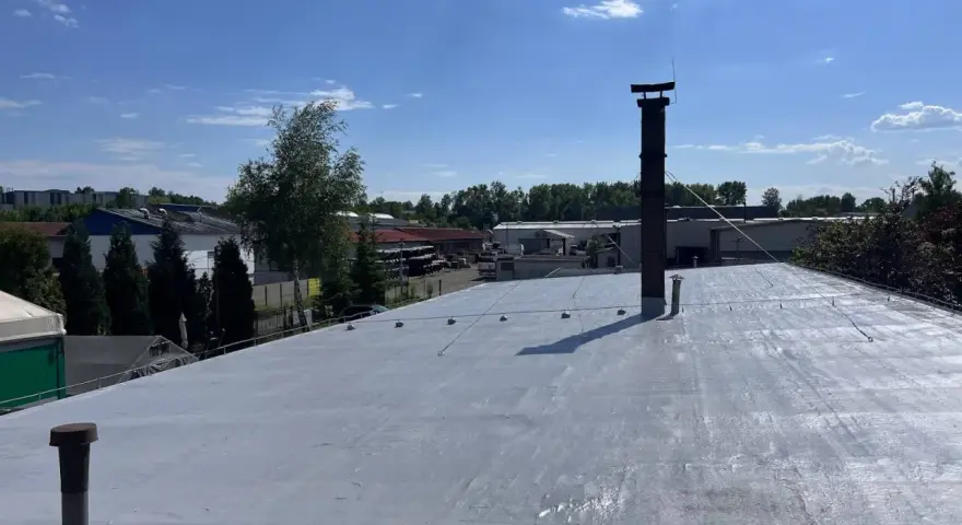 Nowy dach z doskonałą hydroizolacją, gotowy na każde warunki. W tle budynki przemysłowe i błękitne niebo z chmurami.
