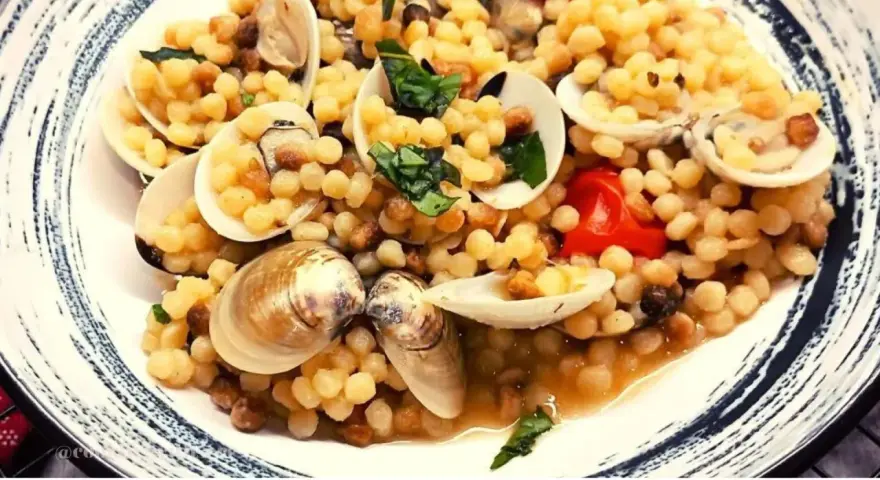 Piatto di fregola con vongole, pomodorini e basilico fresco. Un classico sardo che profuma di mare.