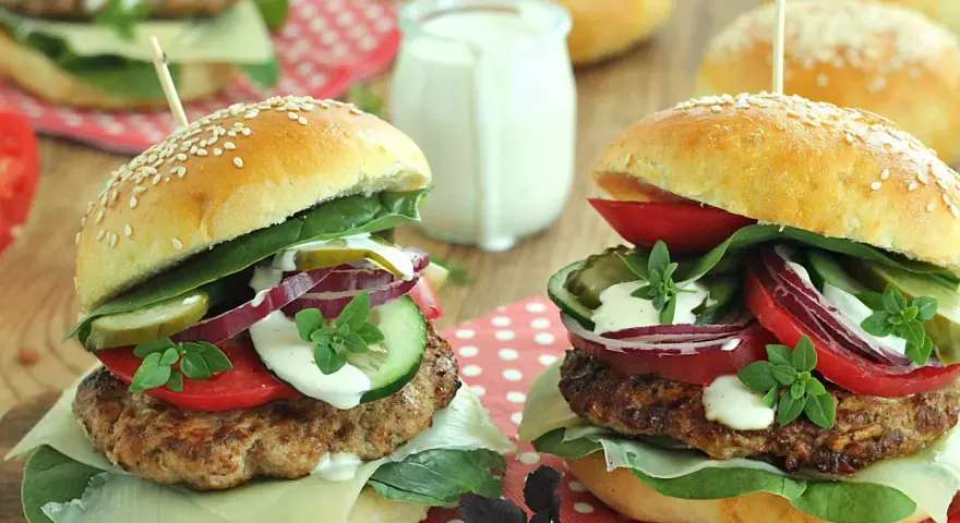 Dwa soczyste burgery wołowe z dodatkami na drewnianym tle.