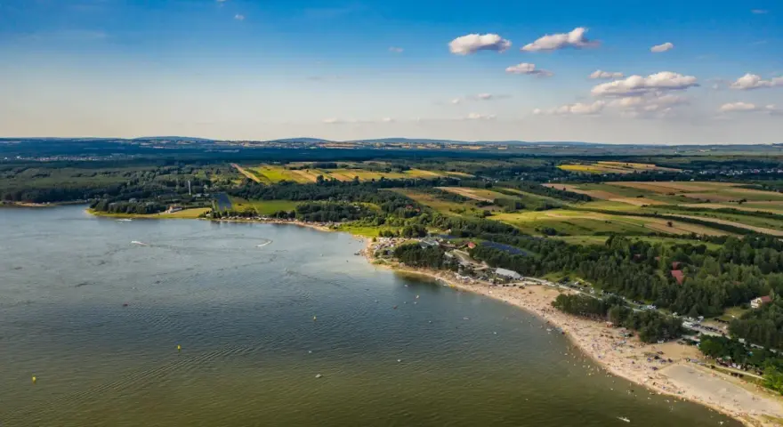 Letnie słońce nad **Jeziorem Chańcza**. Tłumy plażowiczów, zielone lasy i pola tworzą malowniczy krajobraz.