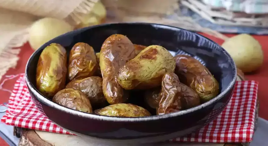 Patate novelle dorate e croccanti, appena sfornate dalla friggitrice ad aria, servite in una ciotola scura su un tagliere di legno.