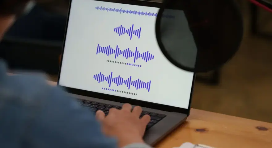 Osoba pracuje przy laptopie, na ekranie widoczne są wykresy fal dźwiękowych, co może być związane z tworzeniem adlibów.
