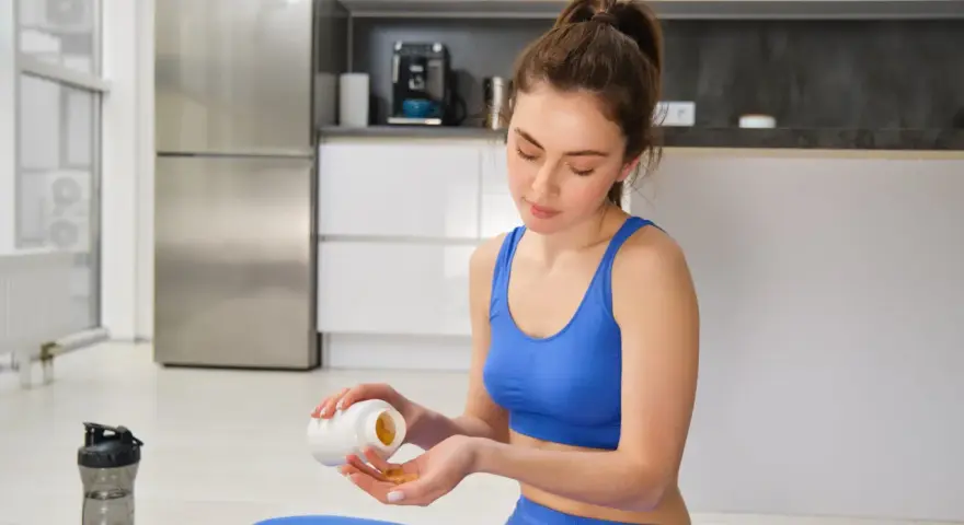 Femme en tenue de sport bleue prend des gélules, espérant un vitamine b12 effet immédiat pour son bien-être.