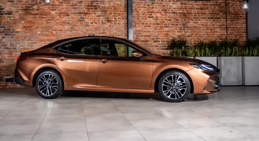 Elegancki, brązowy sedan auto z nowoczesnymi felgami stoi na tle ceglanej ściany.