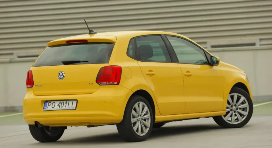 Żółty Volkswagen Polo widziany z tyłu, z widocznym tylnym światłem i tablicą rejestracyjną.