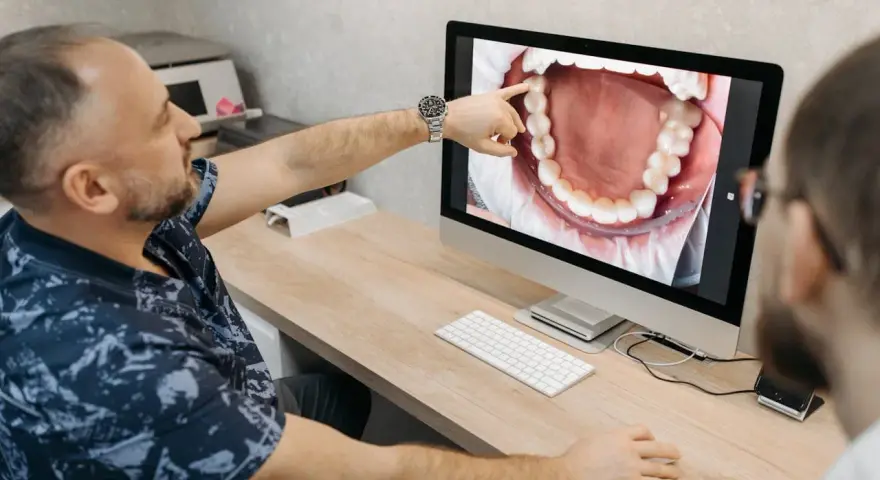 Dentysta omawia z pacjentem czyszczenie kieszonek dziąsłowych, wskazując na zbliżenie jamy ustnej na monitorze.