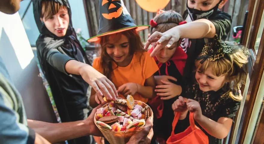 Barn i Halloween-kostymer sträcker sig efter godis ur en korg. Det är en klassisk "bus eller godis"-kväll!
