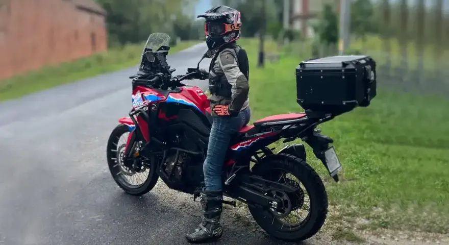 Motocyklistka w kasku i z kufrem na bagażniku gotowa na wyprawę po Kaszubach.