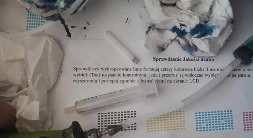 Narzędzia do automatycznego czyszczenia drukarki Brother: strzykawka, papierowe ręczniki z atramentem i instrukcja "Sprawdzenie Jakości druku".