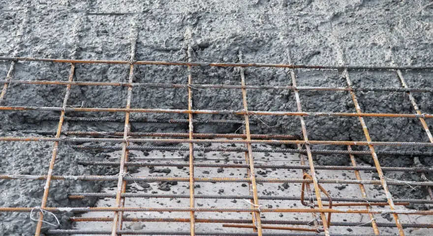 Siatka zbrojeniowa czeka na beton na fundament. Powierzchnia jest szara i chropowata, z widocznymi prętami.