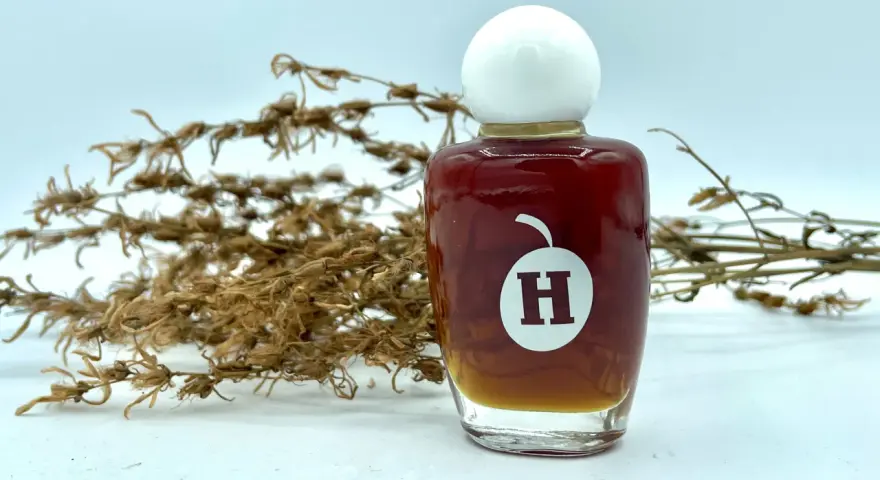 Frasco de aceite de hiperico con tapa blanca, junto a ramas secas.