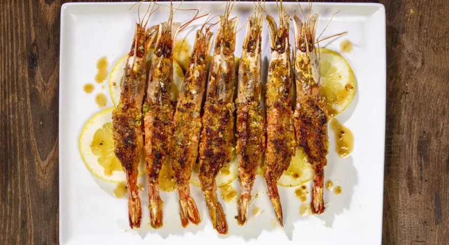 Gamberoni al forno dorati e croccanti, serviti su fette di limone e conditi con un sugo saporito.