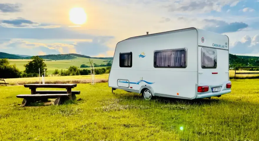 Przyczepa Caravelair zaparkowana na łące o zachodzie słońca. W tle malownicze wzgórza i pola.
