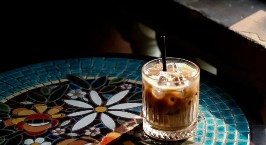 Orzeźwiający cold brew latte z lodem, podany na kolorowym, mozaikowym stoliku, w promieniach słońca.