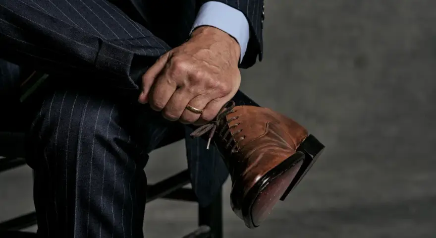Un uomo con un abito gessato blu scuro e una camicia azzurra indossa eleganti scarpe stringate marroni.