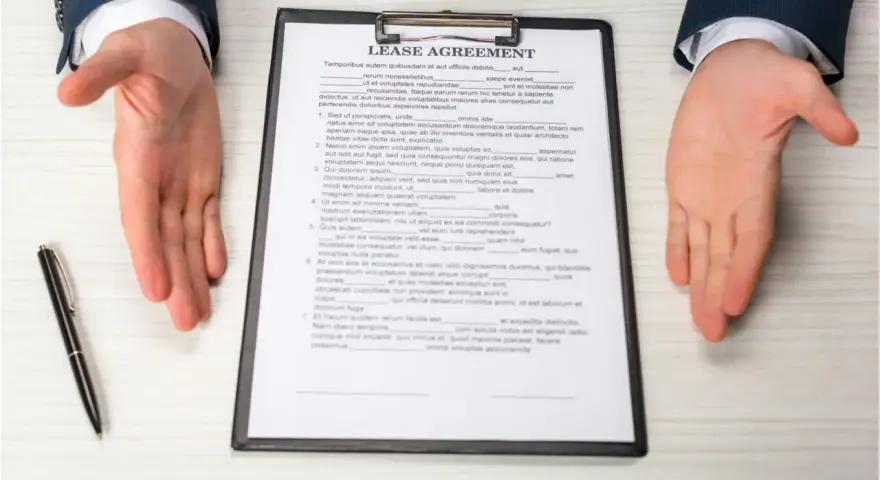 Dłonie wyciągnięte nad dokumentem "Lease Agreement" i długopisem.