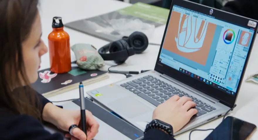 Studentka na studiach grafika Warszawa tworzy projekt na laptopie, używając tabletu graficznego.